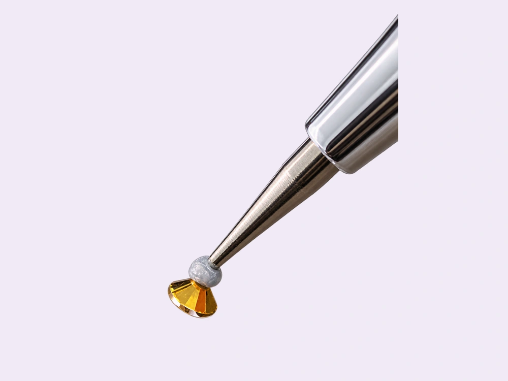 Prepared tip holding one gold rhinestone by its faceted top